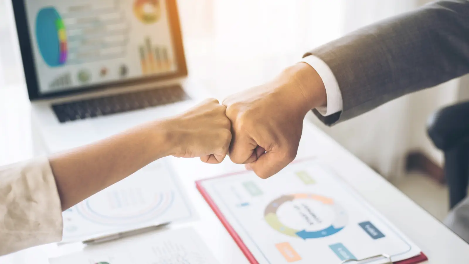 Two professionals doing a fist bump in an office with financial charts on the desk, symbolizing trusted partnership with Naperville Tax Accountant