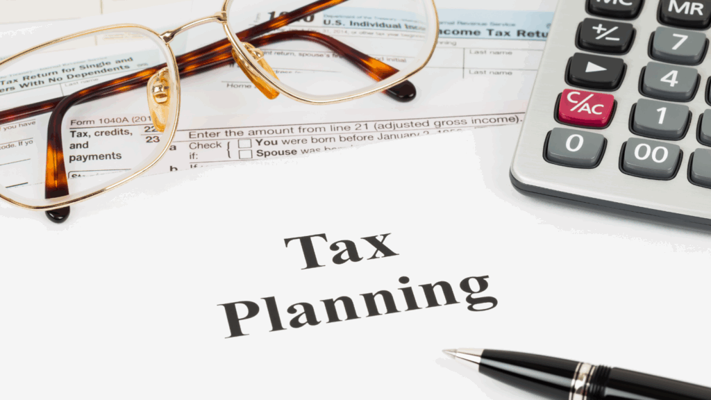 Financial workspace with Tax Planning document, calculator, pen, and eyeglasses on top of IRS tax forms. The image represents expert tax planning services designed to help individuals and small business owners reduce tax liabilities and optimize financial strategies year-round.